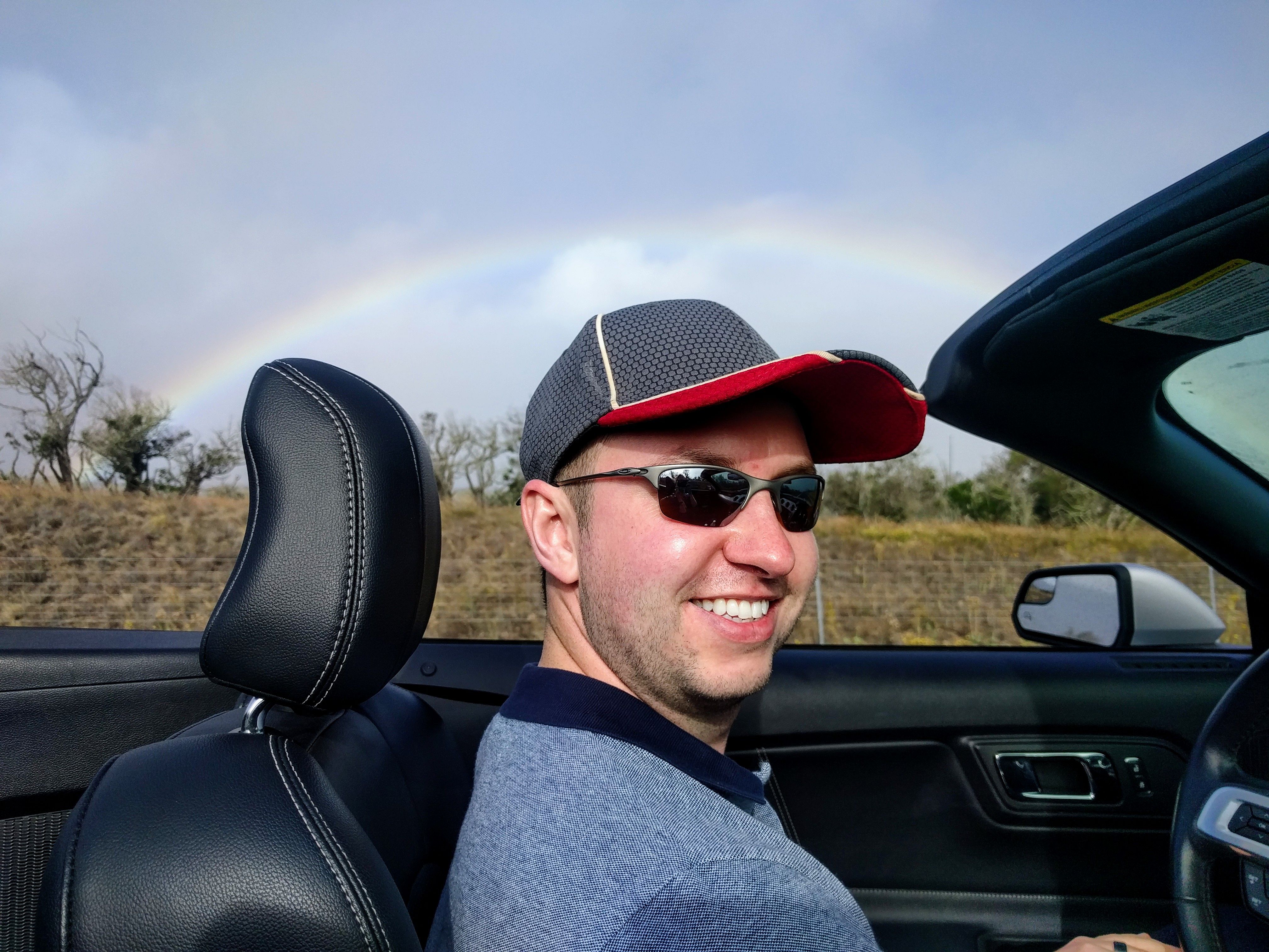 Rainbow in the background of Matt sitting in the car
